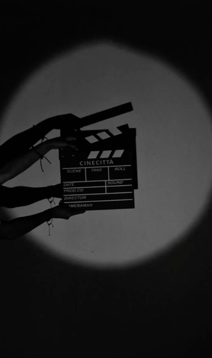 Hands holding a clapperboard inside a circle of light.
