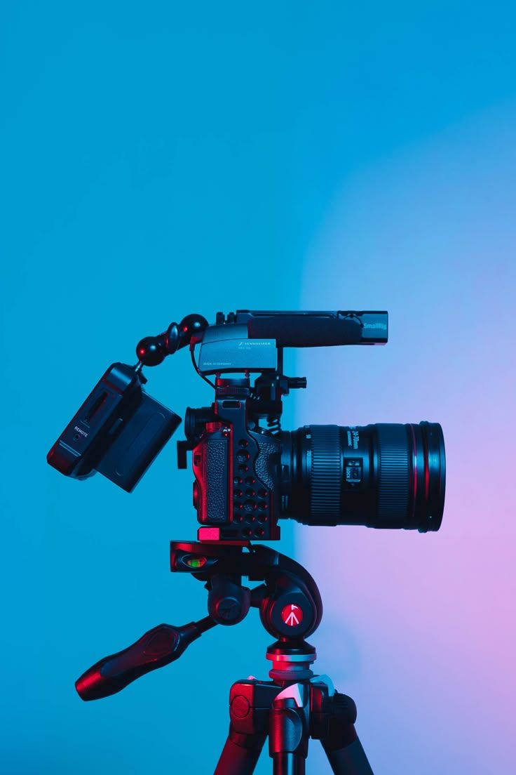 A cinema camera on a tripod against a blue and pink backdrop.